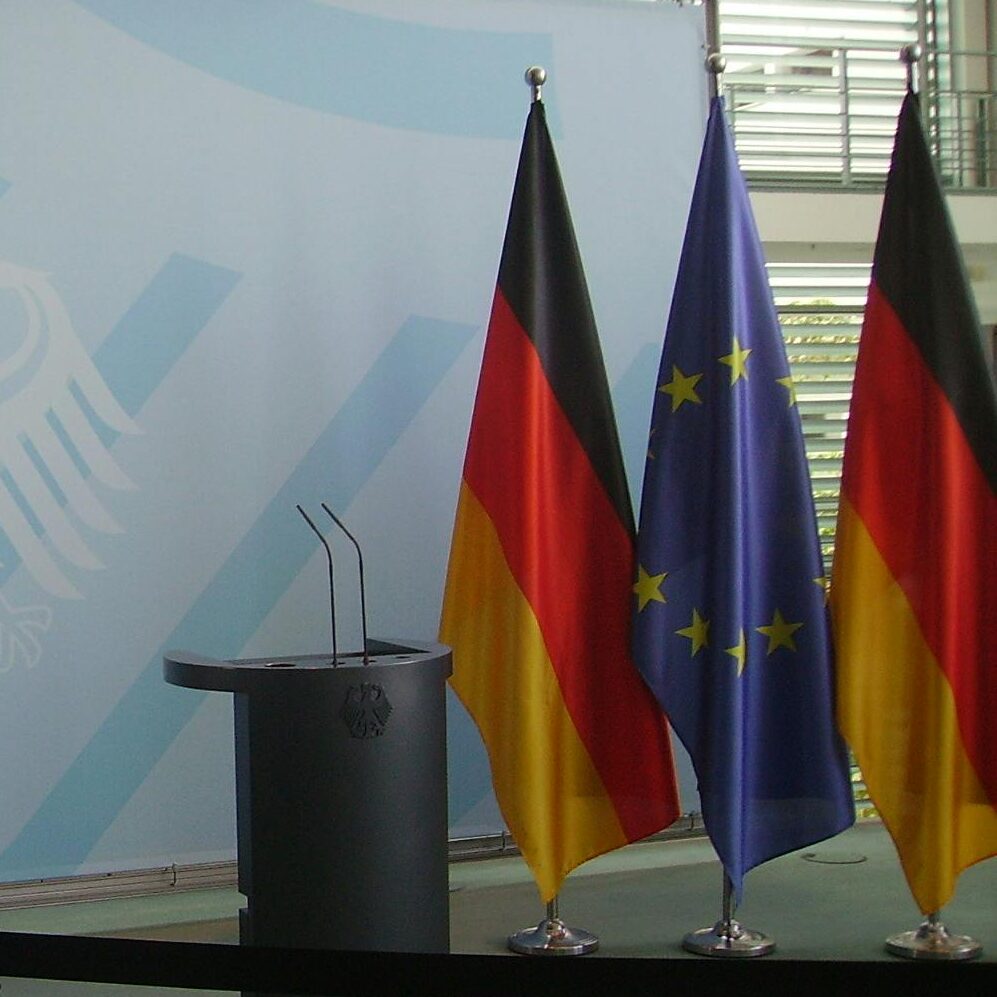 Die Eu-Flagge und die Deutschland flagge stehen neben einem Rednerpult.